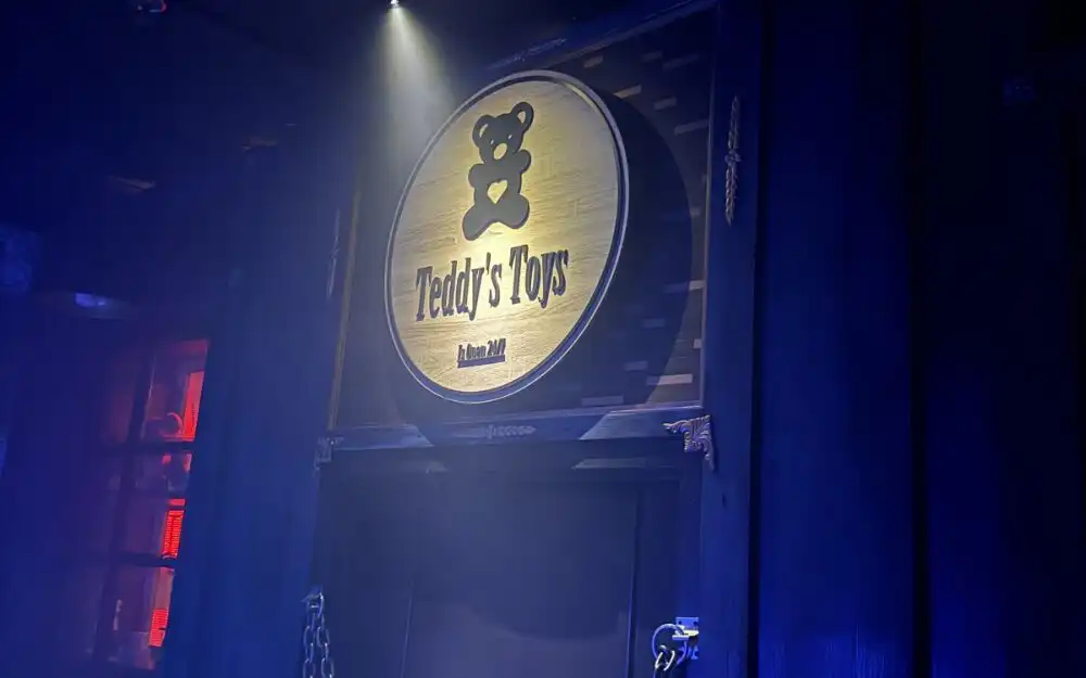 Spotlit wooden Teddy's Toys sign in the dark, mysterious The Missing Toymaker escape room at Huddy's Escape in Ocala, Florida.